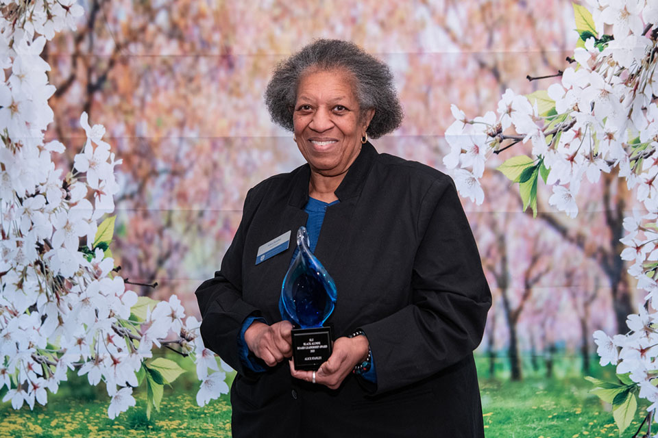 BAA Board Leadership Award 2025 Alice Stanley poses for a photo with an award in front of a floral background.