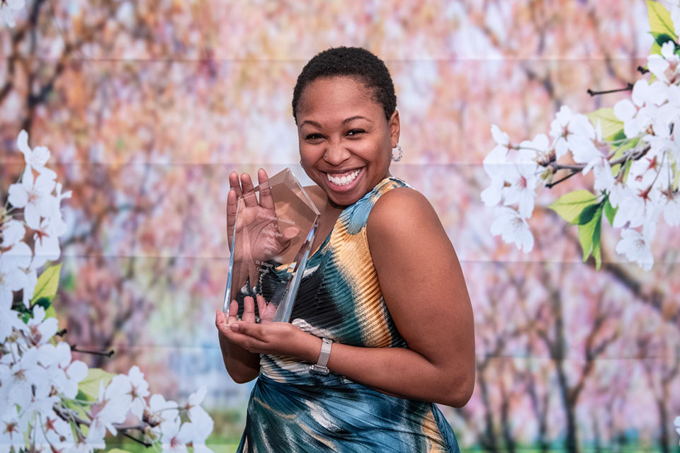 BAA Distinguished Black Alumni Award 2025 Brittany Conors holds an award and smiles for a photo in front of a floral background..