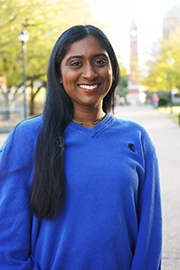 Kirti Madhu A headshot photo of Kirti Madhu with a clocktower and trees in the background.