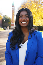 Reueline Arulanandam A headshot photo of Reueline Arulanandam with a clocktower and trees in the background.