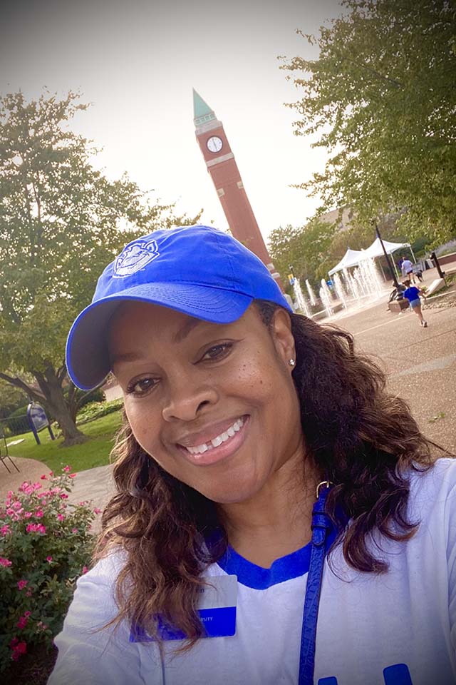 Lydia Pye Huston A woman poses for a selfie outside on campus with a clock tower behind her.