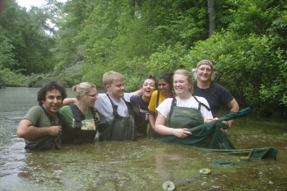 Seven students stand in water, wearing hip waders