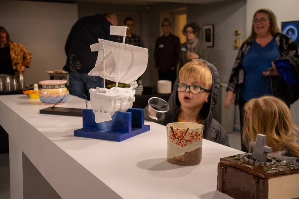 A young art admirer enjoys the SEEDS exhibit A young child examines a piece of pottery in a clear display case.