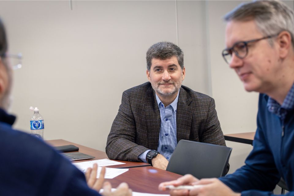 a man in the middle of two other people sits listening at a desk