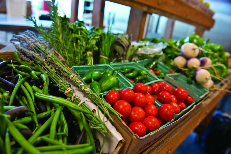 Fresh Gatherings A row of fresh produce in baskets at a market including peppers, tomatoes, onions and greens