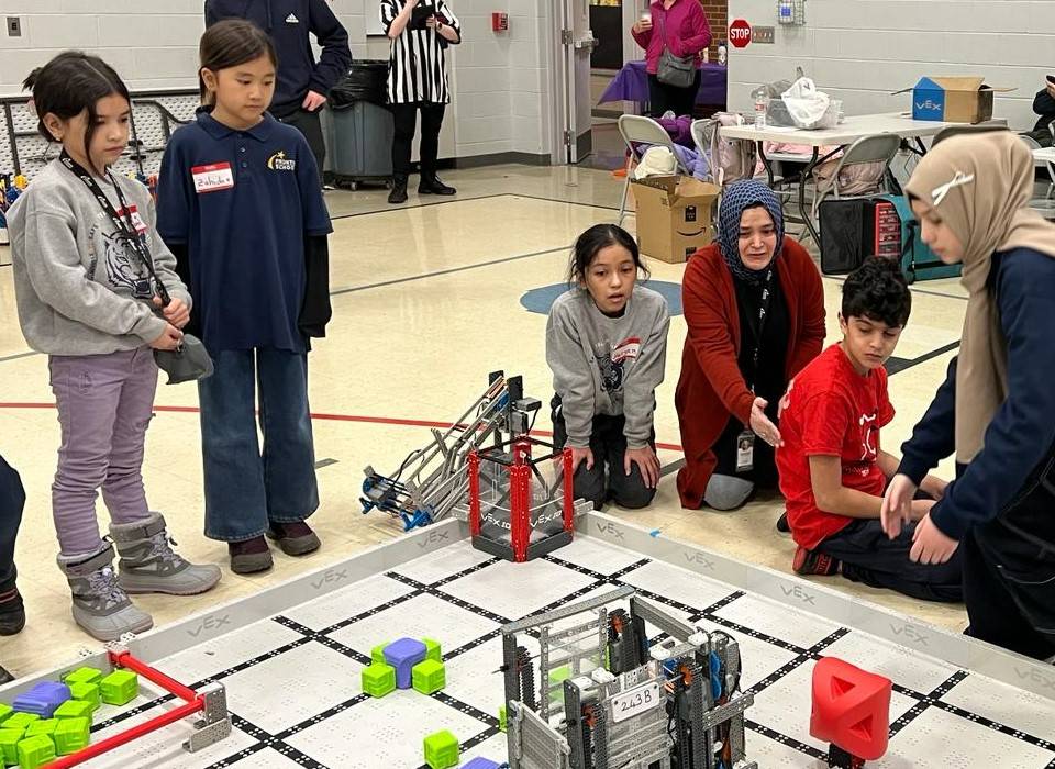Students and adults examine materials on a gym floor during a robotics competition.