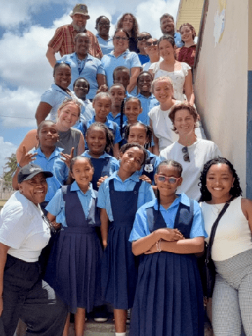 SLU students and professors posing on a stairway with Belizean students and teachers. The Belizean students are wearing blue school uniforms.