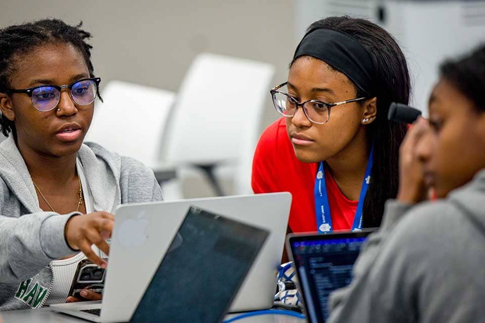 Two female students work together on a laptop in a classroom.
