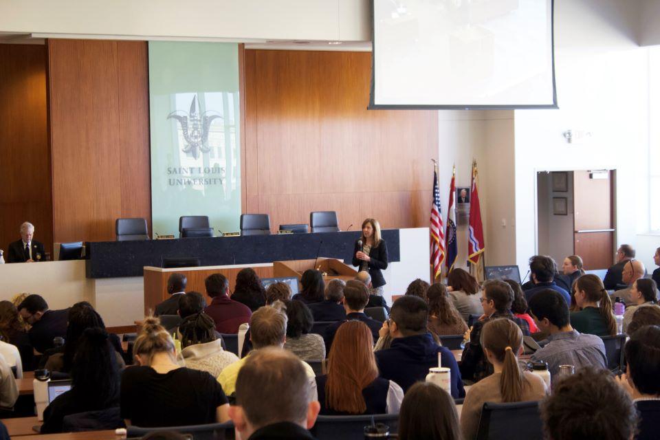 the image shows a crowded courtroom at Scott Hall Audience members are seen from behind as a speaker talks at the front of a lecture hall.