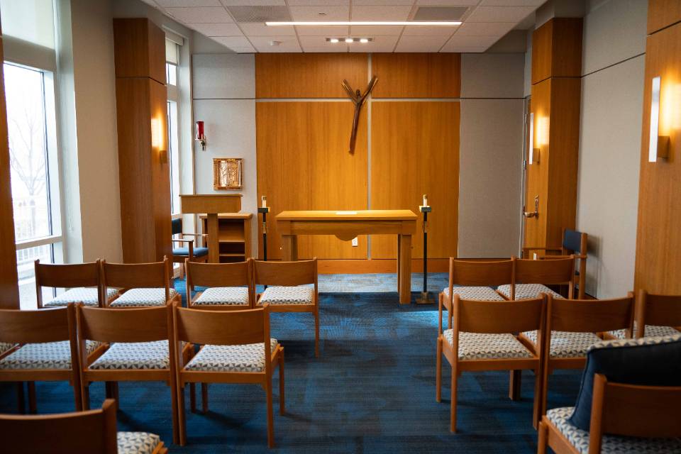 Spring Chapel Chairs are seen in rows from behind with an altar at the front of the room. An abstract, modernist crucifix is on the wall.