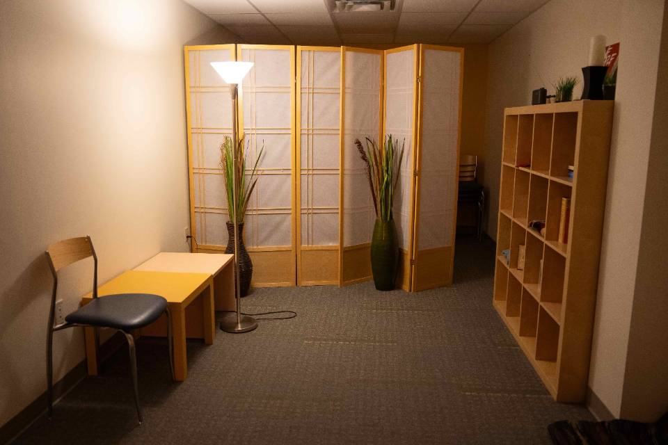 Wuller Interfaith space A small room has a table and chairs along one side and a large wooden set of cubbies along the other wall, and a screen that goes partially across the far wall.