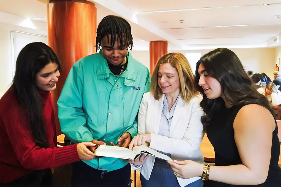 Business and Economics One student is reading a book while other student is talking with the professor in the background.