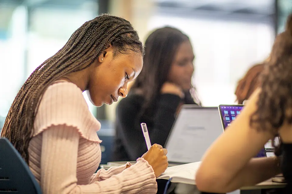 A student sitting at a table writing in her notebook in the student lounge.