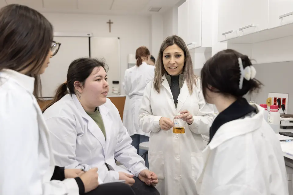 Three students and a professor have a discussion while sitting around an outdoor table with a laptop.