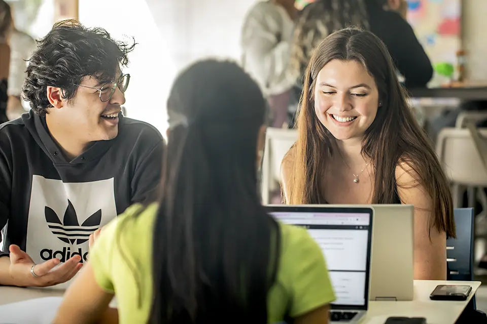 three students sitting at a table with theirs laptops