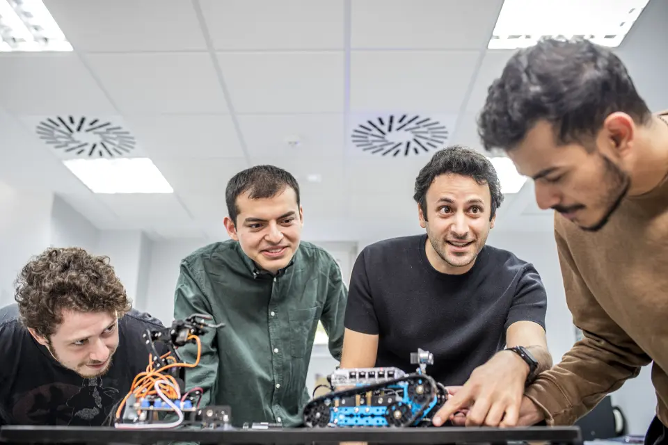 A group of students with their teacher observe a small robot on a table.