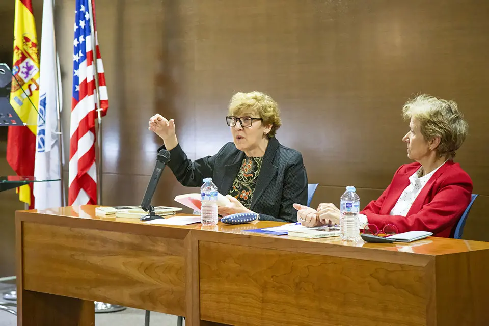 Simposio anual de Español Two women sitting at a table and debating with 3 flags behind them