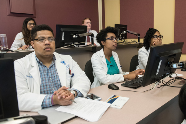 A group of students sit in a SLU classroom. They're listening attentively while working on computers.