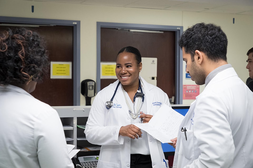 Med Students Three students wearing doctors' coats and stethoscopes stand in a hospital and talk.