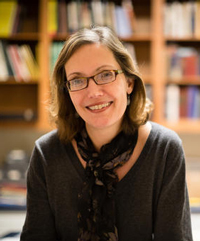 Ena Heller Ena Heller smiles, seated in a library with books on shelves behind her