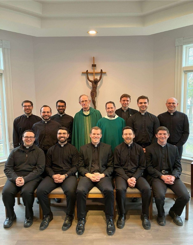 Jesuits in Formation Installed in Ministries A group of Jesuits in formation gathered in a religious ceremony, receiving their ministry assignments. They stand in a solemn setting, dressed in traditional clerical attire, symbolizing their commitment to service and faith.