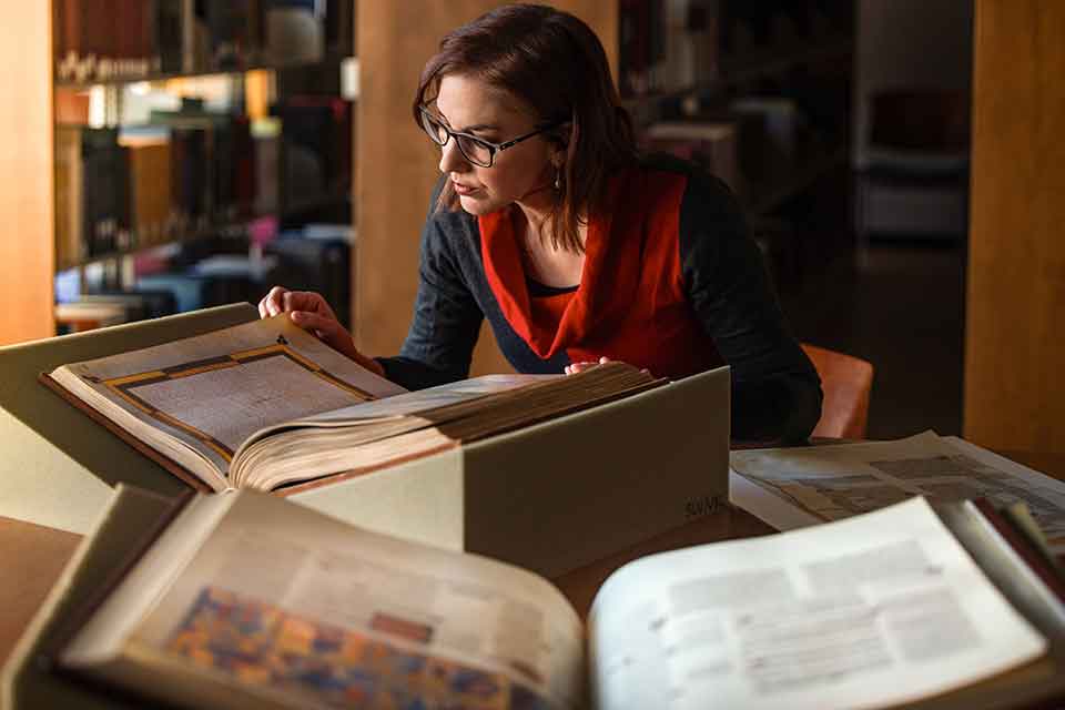Research recruitment A woman examines several large manuscripts that are laid out in front of her
