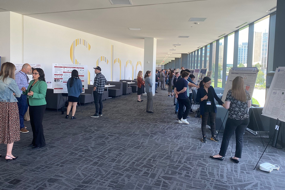 Forum attendees visit with student researchers during the poster session. A corridor is lined with easels containing posters, while forum attendees look at the posters and have discussions.
