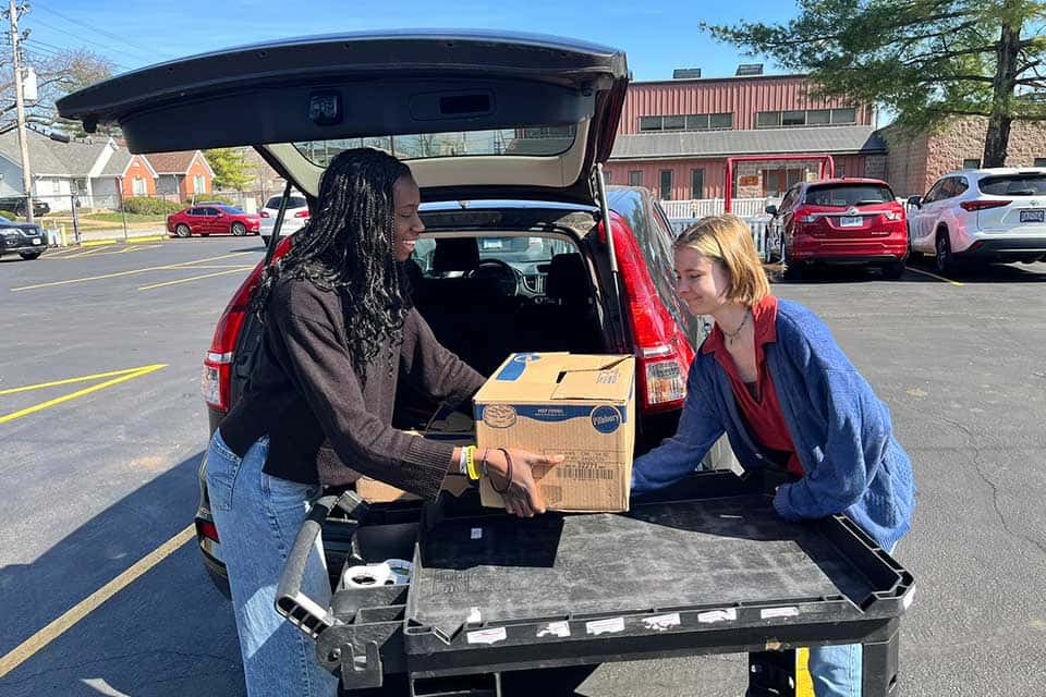 Feeding Families Two female volunteers load the trunk of a car with a box of food to be delivered.