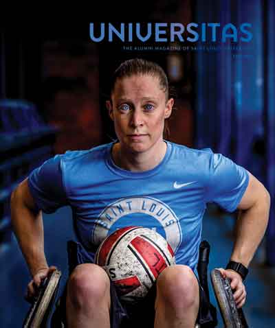 The cover of the 2024 fall issue of Universitas magazine, with an image of paralympian Sarah Adam, wheelchair rugby player. She wears a SLU t-shirt, and has a rugby ball on her lap with her arms on the wheels, ready to go.